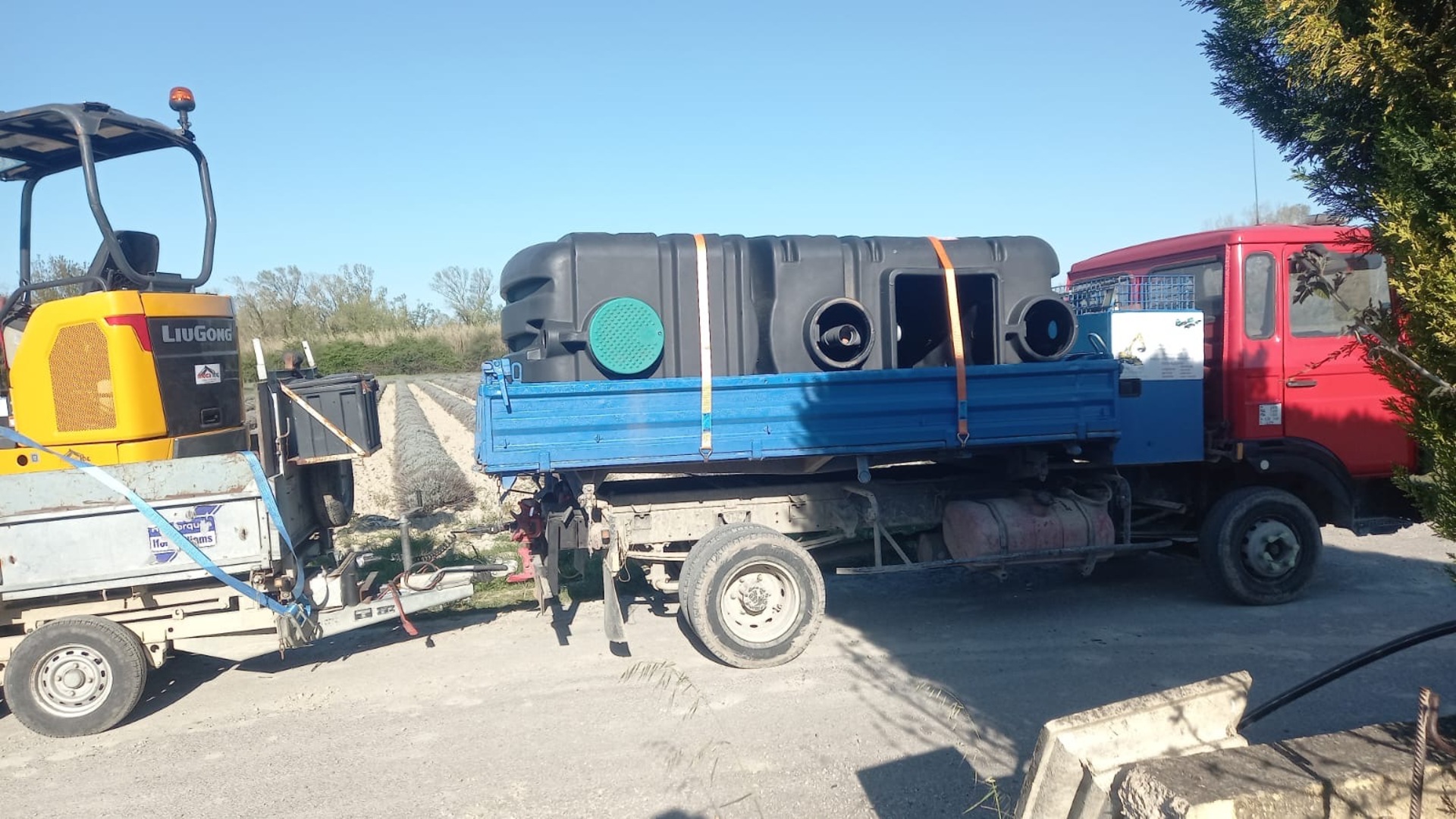 Camion plateau LBTP transportant un mini-pelle et une citerne sur chantier