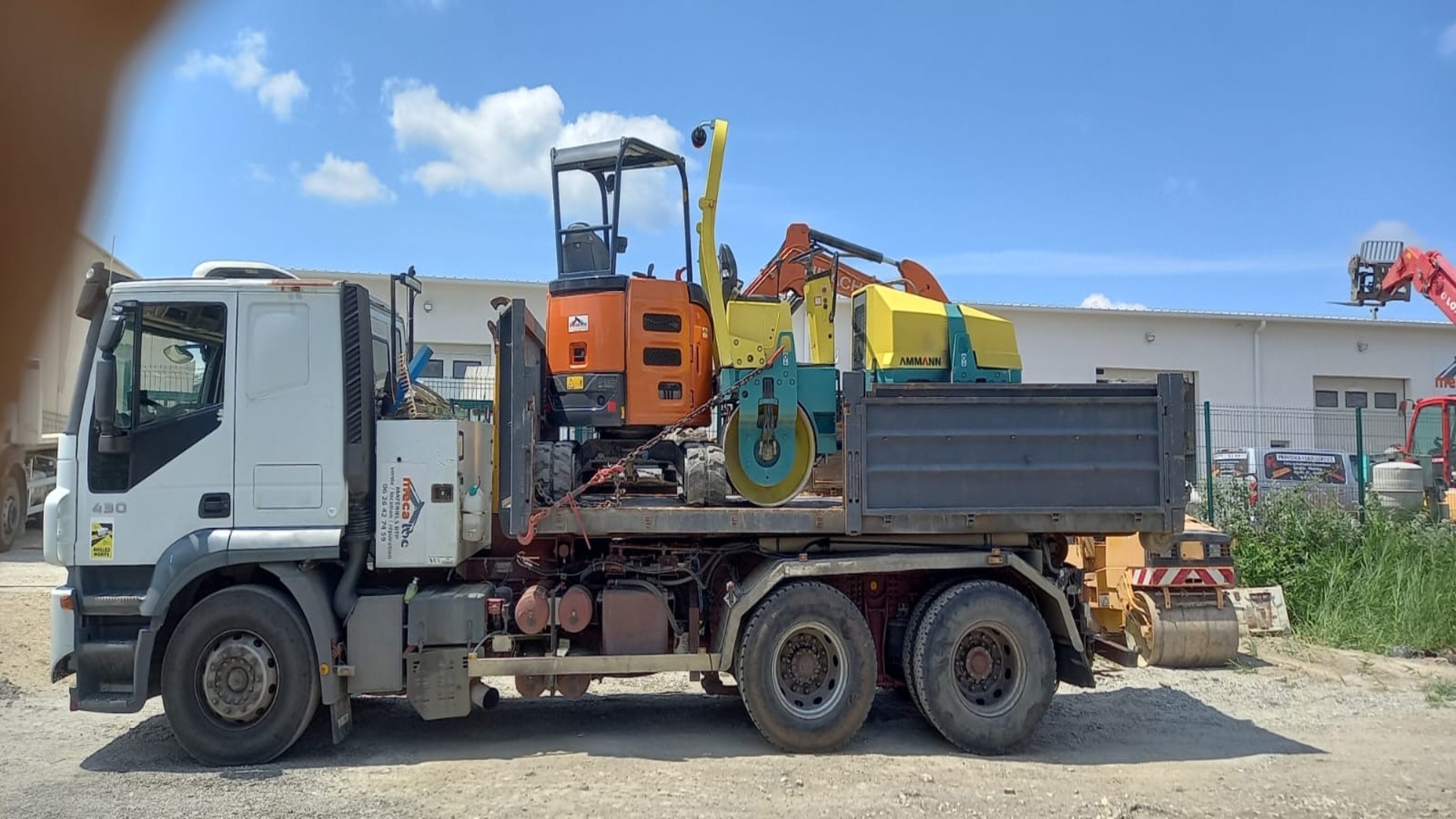 Camion LBTP Tous Travaux transportant un mini-pelle et un compacteur sur chantier
